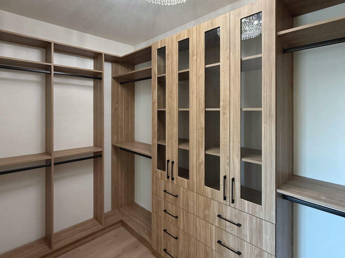 Wood-look walk-in closet with glass-front cabinets, drawers, open shelving and hanging rods.