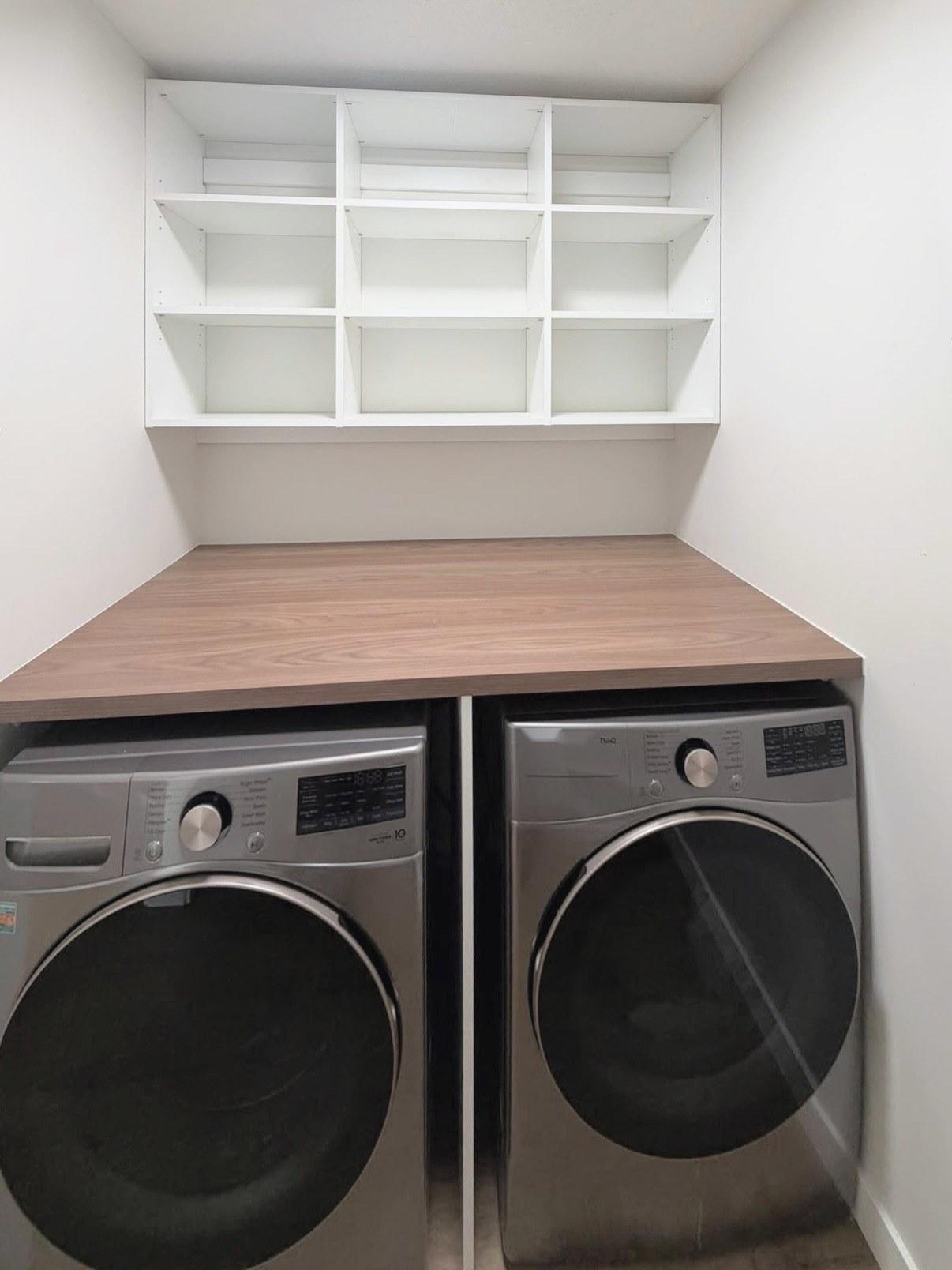 White open shelving above a wood-look counter and two laundry appliances.