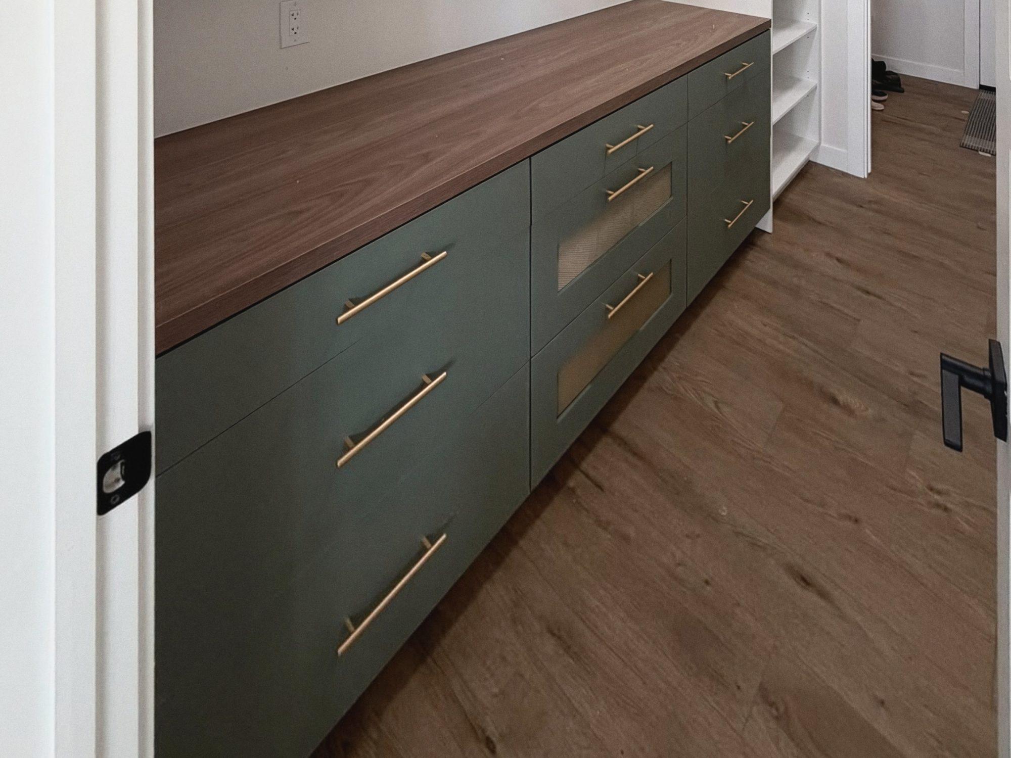 Open white shelving above a run of green lower cabinets with drawers and a wood-look countertop.
