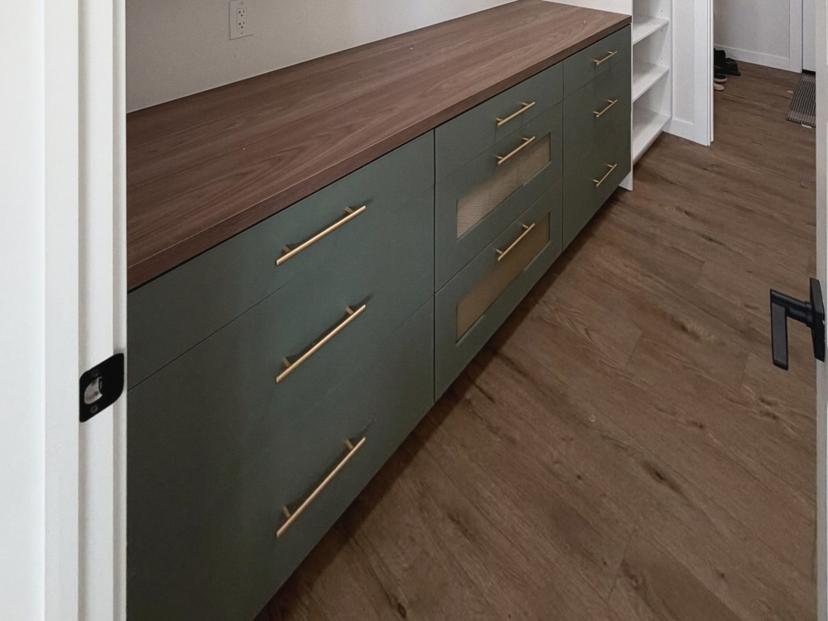 Open white shelving above a run of green lower cabinets with drawers and a wood-look countertop.