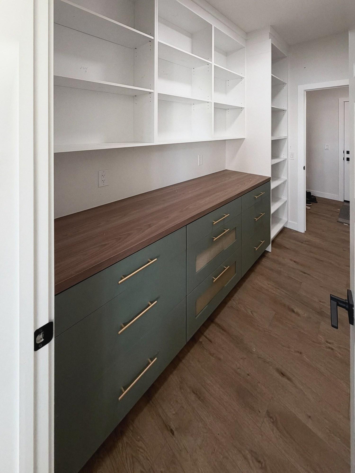Green lower cabinets with drawers beneath a wood-look counter and white open shelves.
