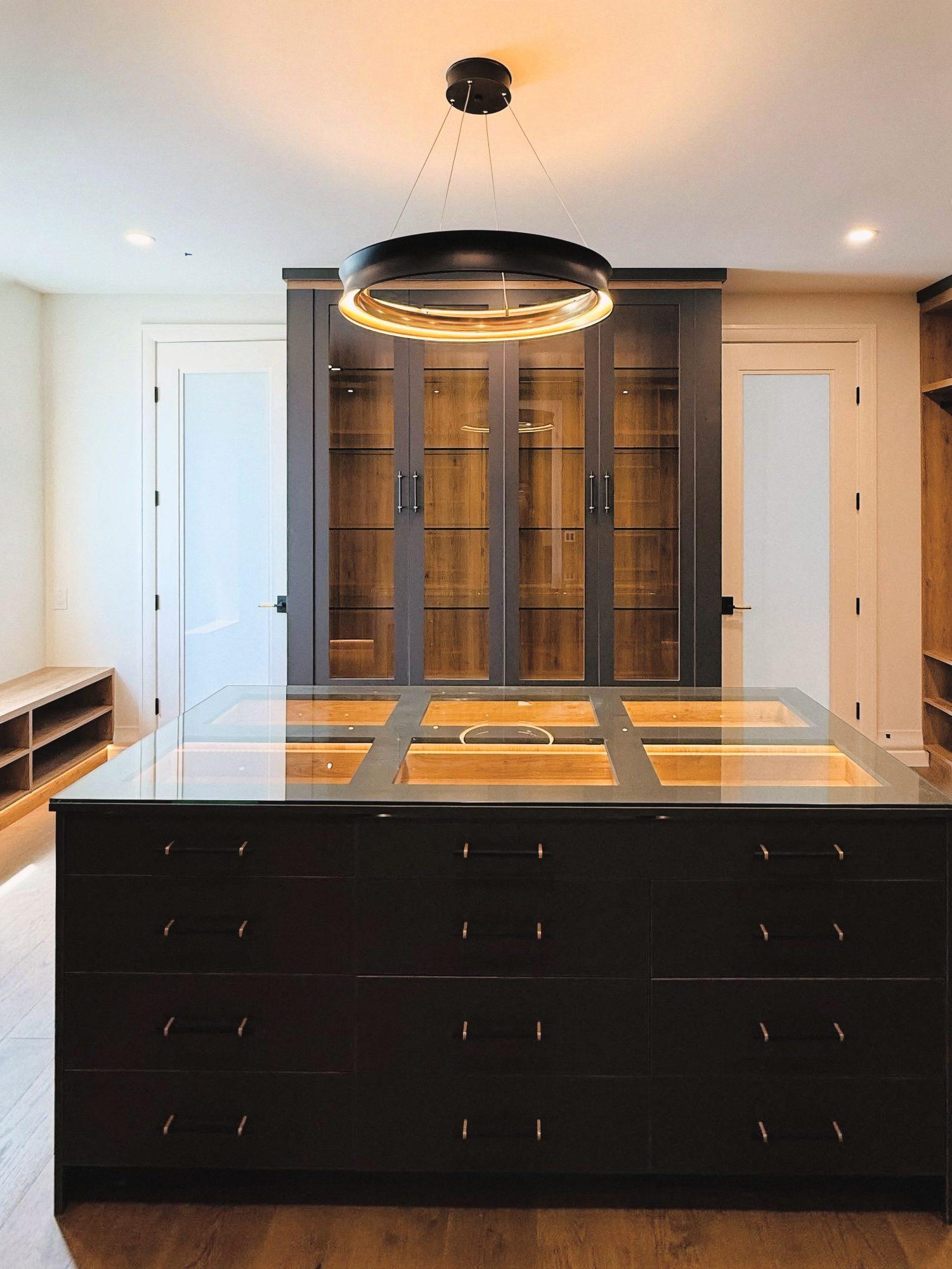 Dark closet island with drawers and a glass top in front of glass-front cabinets.