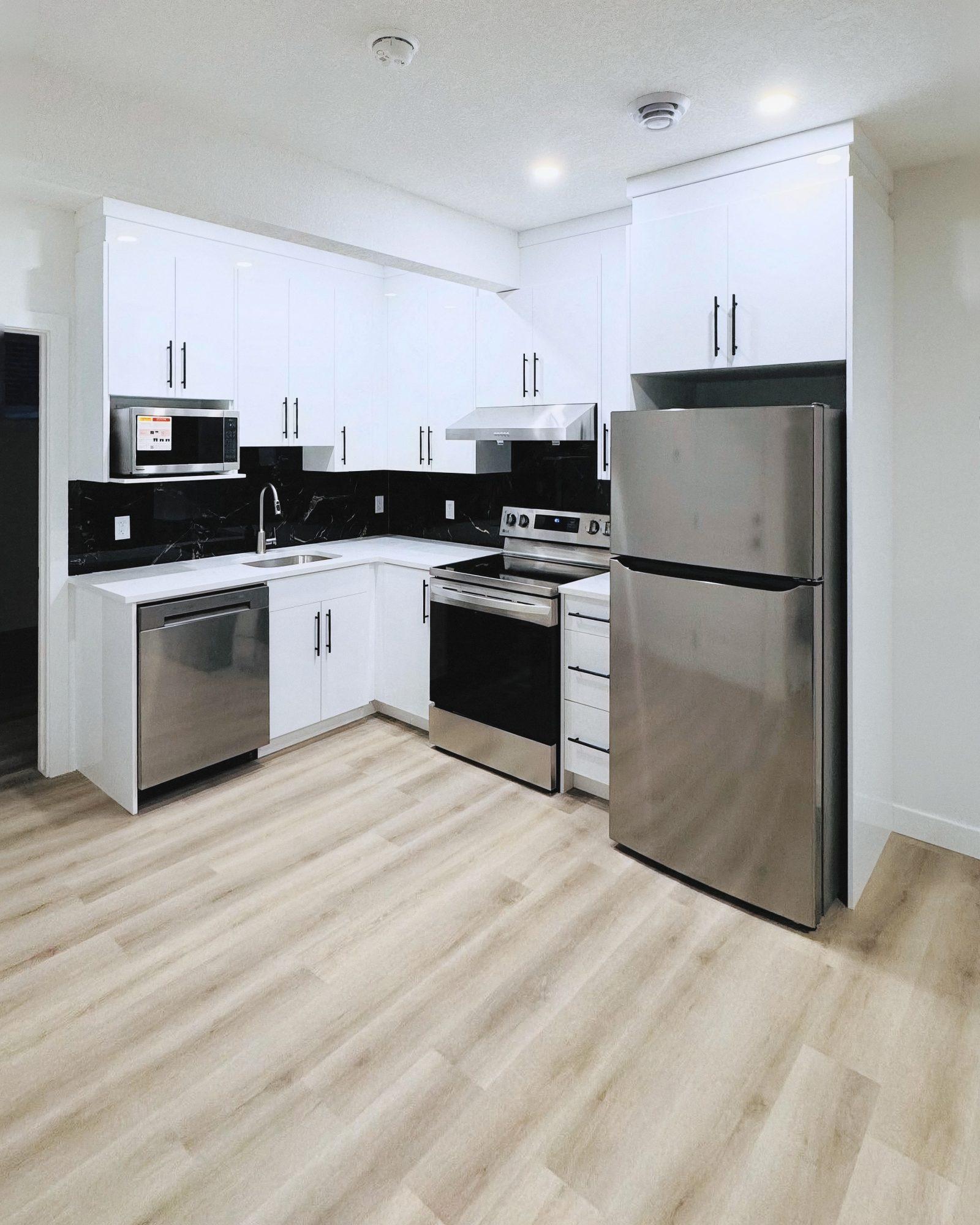 White kitchen with upper and lower cabinets and black handles.